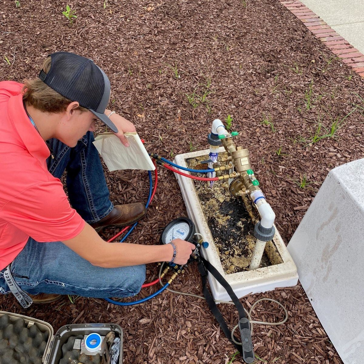 Town of Clayton Intern kneels beside water meter, checking guages and pipes.