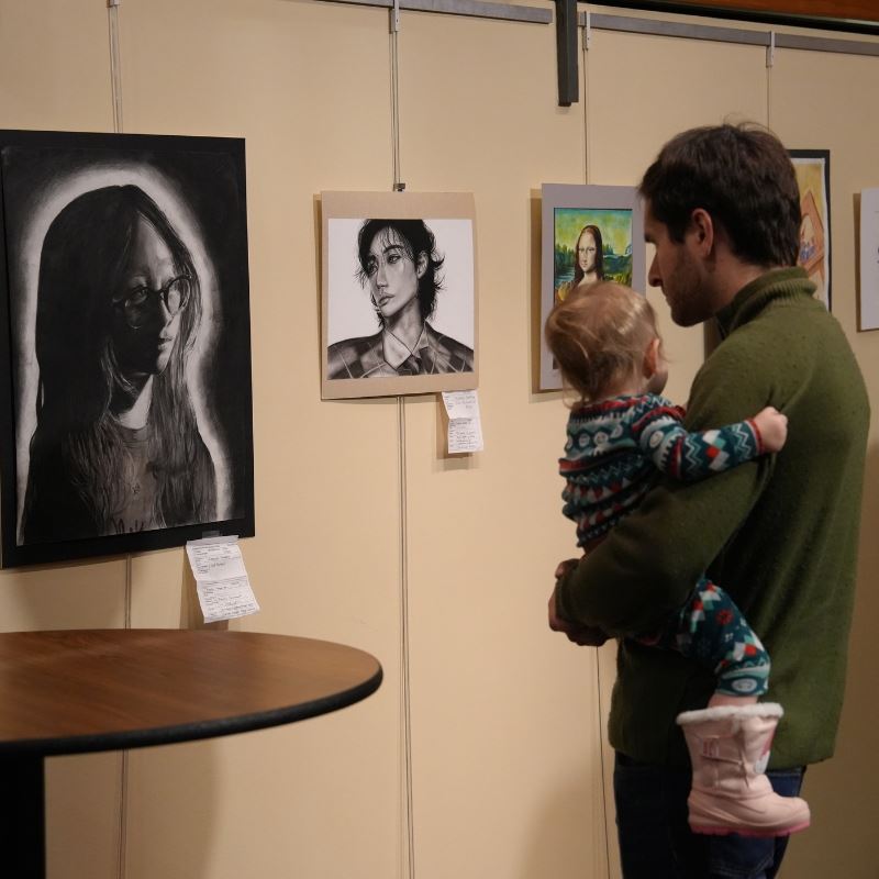 Man holds young child while looking at student art in Town Hall